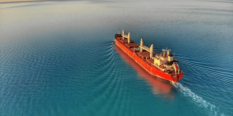 A red cargo ship sails on a blue ocean.