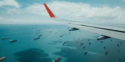 View from aircraft wing overlooking cargo ships at sea, representing Caroz' air and ocean freight services.